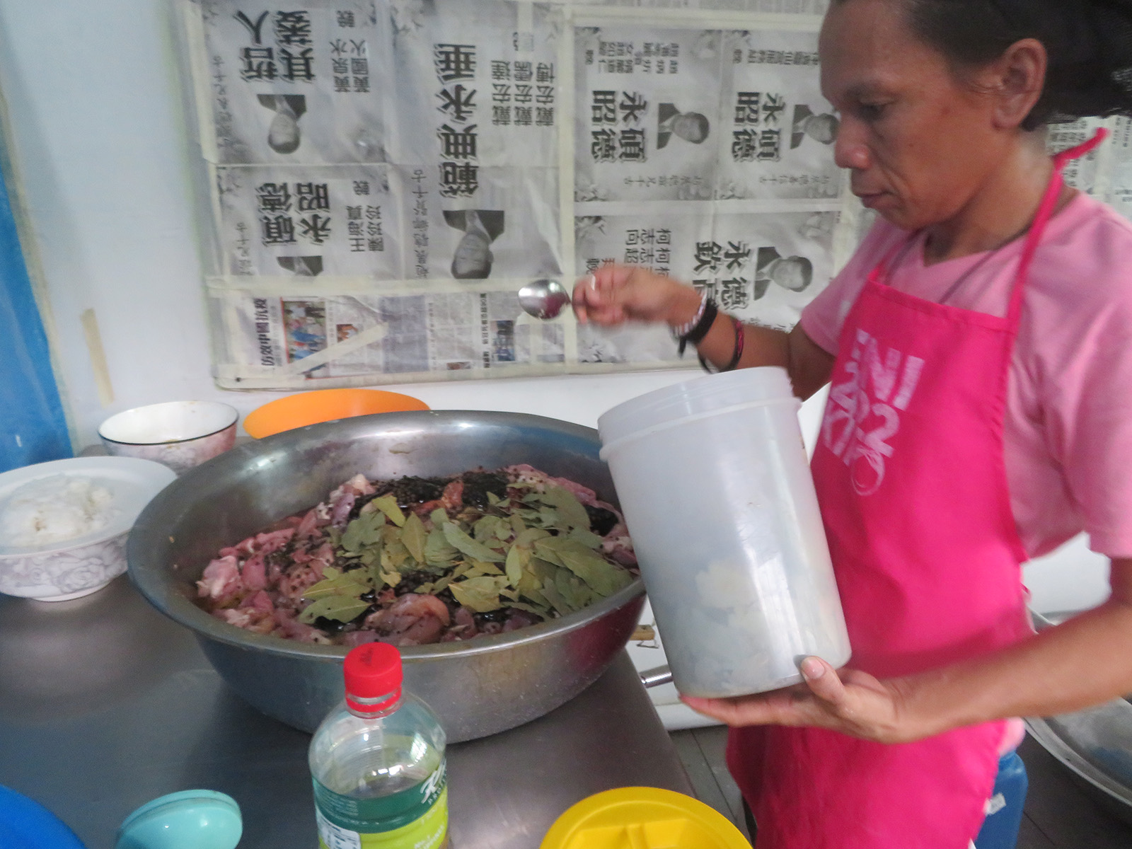person in a pink apron seasoning a large pot of food
