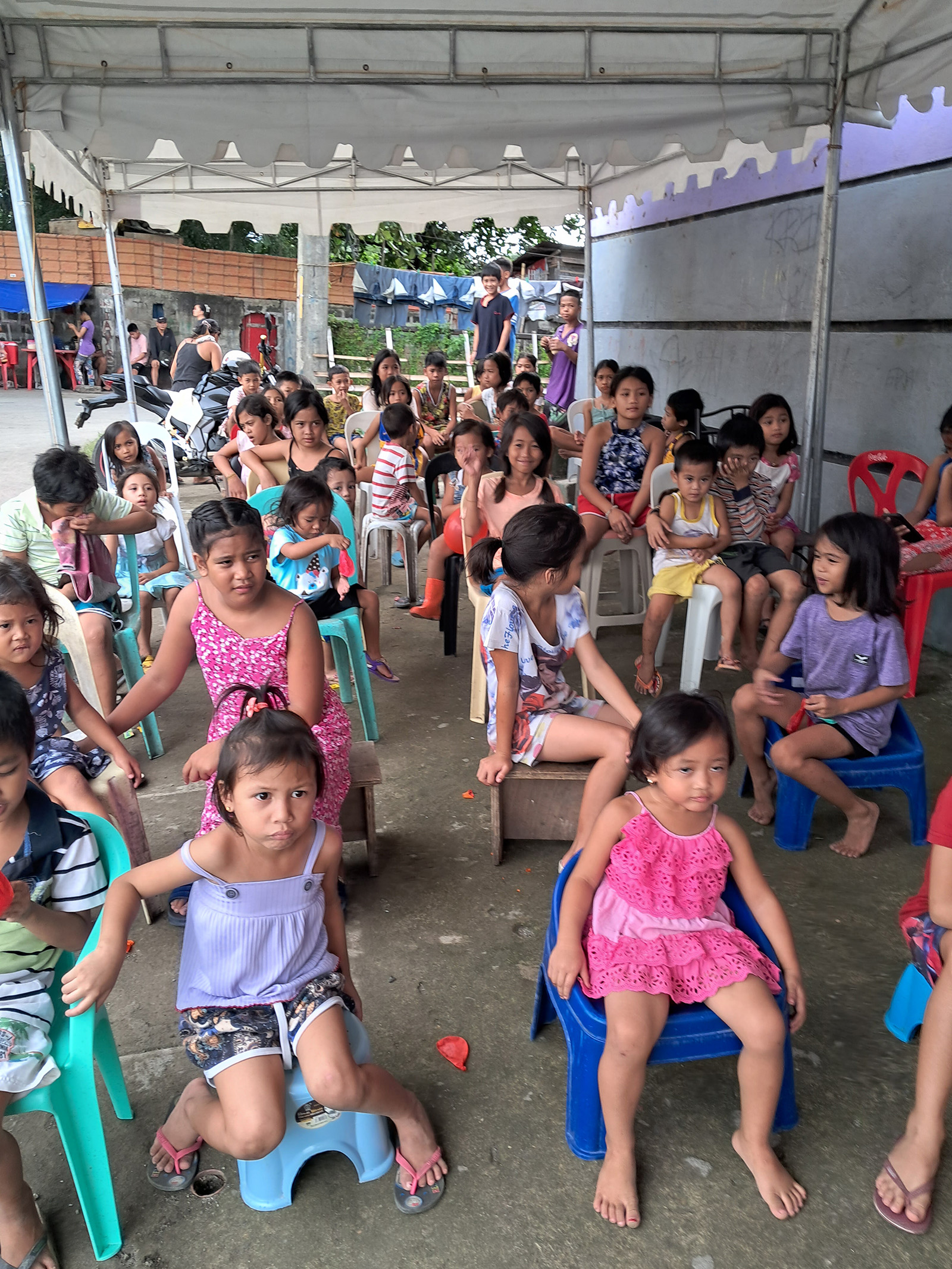 Children seated in rows under an awning