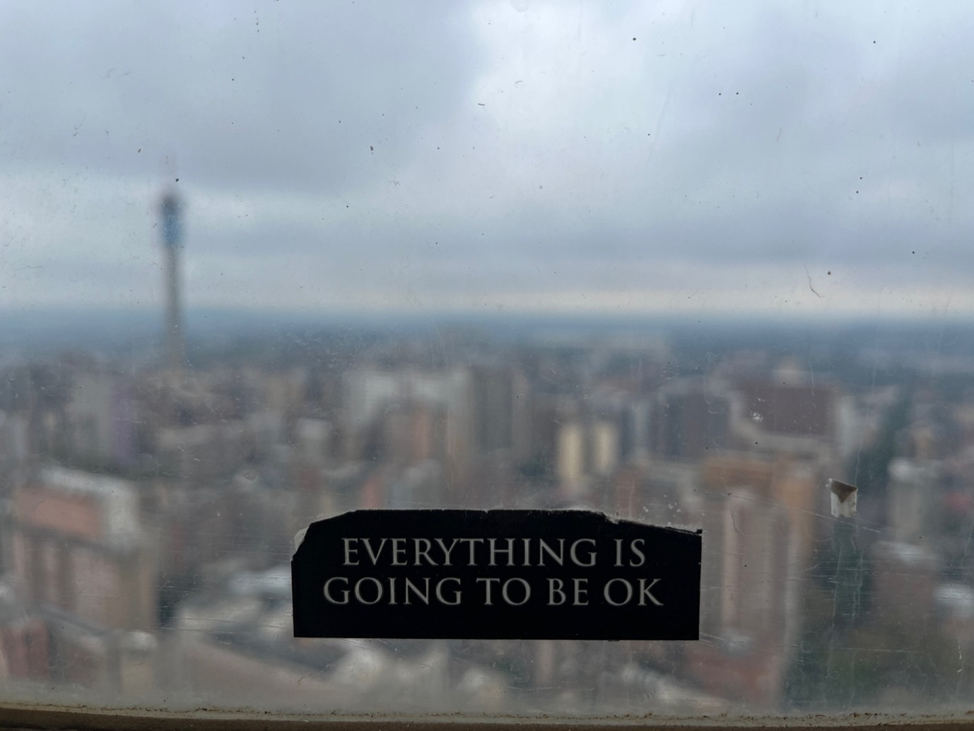 Blurred view of a city through a window, with the phrase 'Everything is going to be ok' taped onto the window